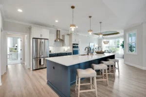 Modern kitchen with white cabinets, navy island, gold lights, and stainless steel appliances.