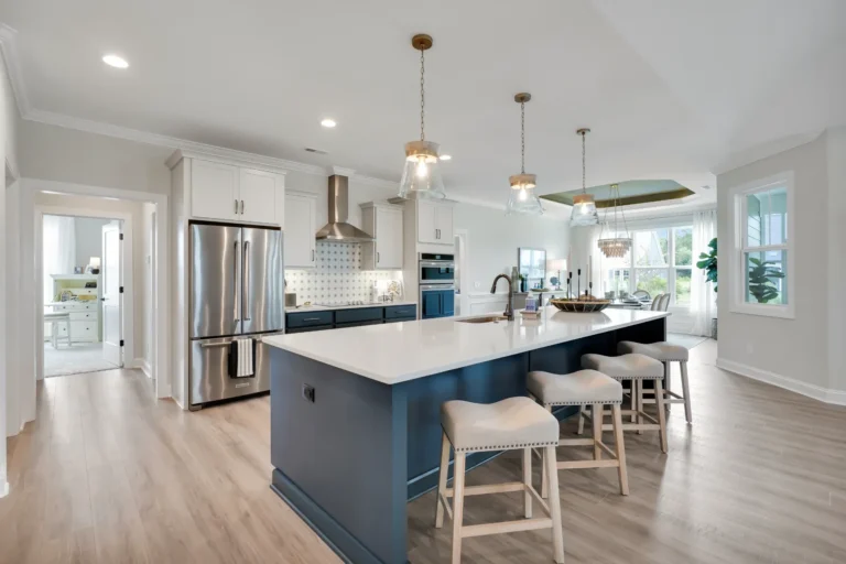 Modern kitchen with white cabinets, navy island, gold lights, and stainless steel appliances.