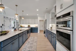 Modern navy and white kitchen with quartz island, gold pendant lights, and light wood floors.