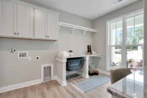 Bright modern laundry room with workspace, natural light, wood floors, and white cabinets.