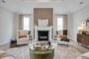 Cozy neutral living room with white fireplace, plaid chairs, green ottoman, and elegant décor.