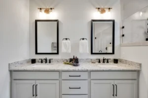 Modern gray double vanity bathroom with granite countertop, black fixtures, and elegant lighting.