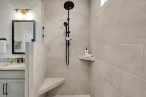 Modern walk-in shower with light gray tiles, black fixtures, and a built-in corner bench.
