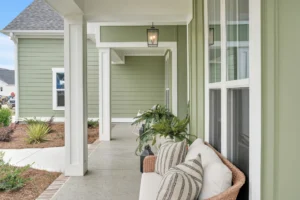 Modern farmhouse porch with sage green siding, white trim, and cozy wicker seating.