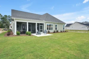 Modern single-story suburban home with covered patio and spacious green backyard under a bright sky.
