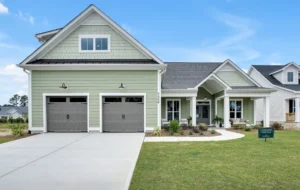 Modern green suburban home with white trim, double garage, and inviting front porch.