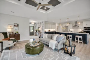 Modern open-concept living room and kitchen with gray sofa, olive ottoman, and navy island.