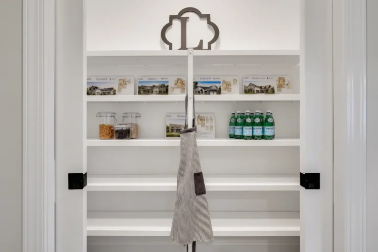 Minimalist white pantry with open shelves, glass jars, green bottles, and a hanging striped apron.