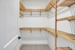 Bright modern walk-in closet with white walls, light wood shelves, and beige carpet flooring.
