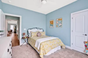 Bright blue bedroom with yellow bedding, white metal bed, and cozy cheerful decor.