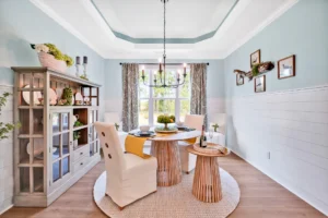 Coastal farmhouse dining room with natural light, round wooden table, and white upholstered chairs.