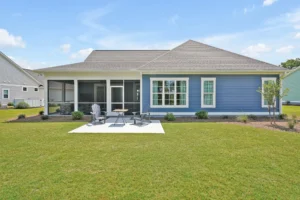 Modern blue single-story house with patio, lawn, and screened porch in a sunny backyard.