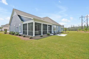 Modern blue-gray single-story home with screened porch and large manicured lawn under clear sky