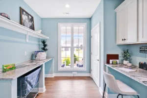 Bright coastal blue flex room with window workspace, white cabinets, and warm wood flooring.