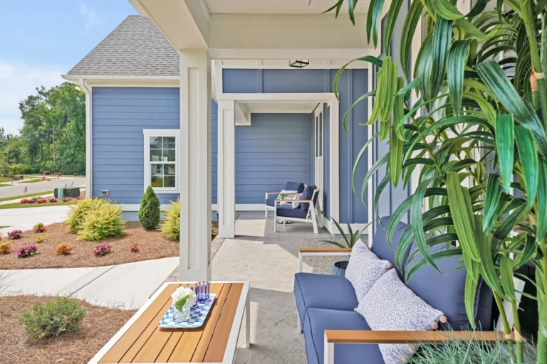 Coastal blue front porch with comfy seating, wooden table, and lush green plants.