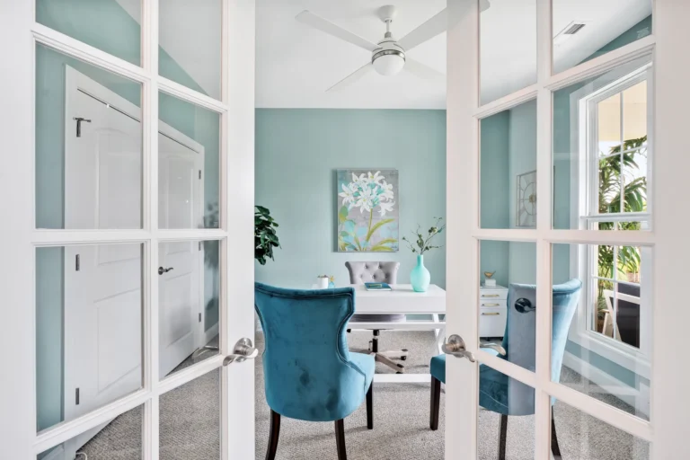 Bright coastal home office with turquoise walls, white desk, and natural light through French doors.