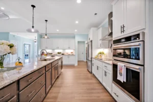 Modern white kitchen with quartz island, pendant lights, stainless steel appliances, and light wood floors.