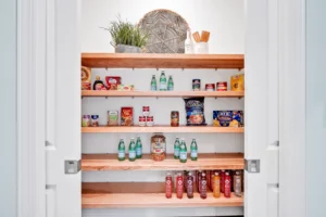 Modern light wood pantry with organized shelves, drinks, jars, snacks, and decorative accents.