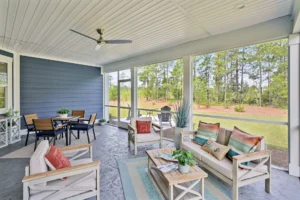 Coastal screened porch with light wood furniture, neutral cushions, and serene forest views.