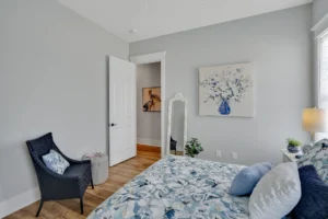 Cozy modern gray and blue bedroom with floral bedding, hardwood floors, and soft natural light.