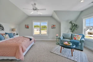 Bright modern bedroom with pastel decor, pink bedding, blue chair, and natural light.