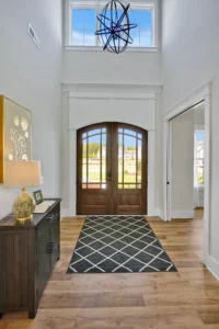 Modern entryway with double wood doors, natural light, patterned rug, and elegant minimalist decor.