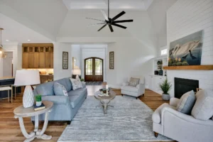 Bright coastal living room with gray furniture, white brick fireplace, hardwood floors, and vaulted ceiling.