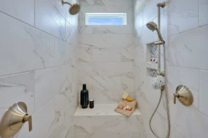 Luxury marble dual shower with bronze fixtures, spa bench, and natural light ambiance.