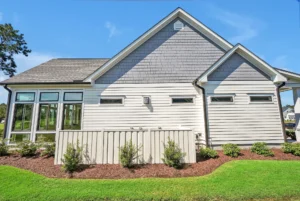 Modern gray suburban house with large windows, white trim, and neatly landscaped green lawn.