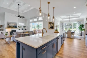 Bright modern coastal kitchen and living room with navy island, wood floors, and natural light.