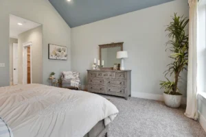 Modern neutral bedroom with blue ceiling, natural light, rustic dresser, and cozy beige bedding.