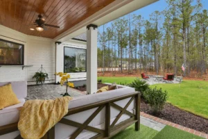 Covered patio with yellow accents overlooking lush backyard and fire pit surrounded by red chairs.