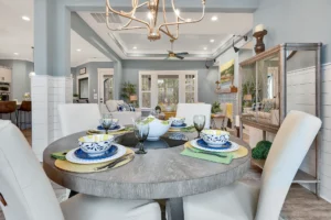 Coastal blue-gray dining room with round table, cream chairs, and elegant gold chandelier.