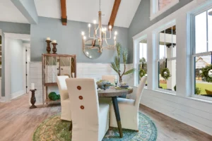 Bright modern farmhouse dining room with wooden table, cream chairs, and exposed ceiling beams.