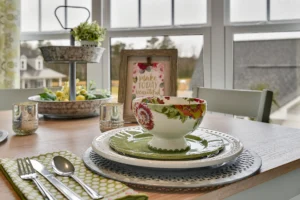 Bright spring dining table with floral dishes, greenery centerpiece, and natural light from large windows.