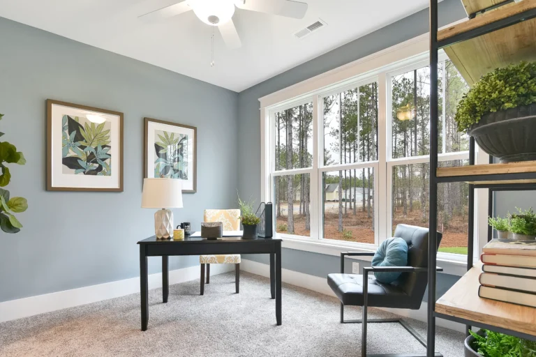 Bright modern home office with black desk, large window, blue-gray walls, and natural light.