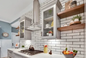 Modern kitchen with white subway tile backsplash, stainless steel hood, gray cabinets, and wood shelves.