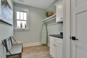Bright modern laundry room with white cabinets, light wood floors, and natural sunlight.