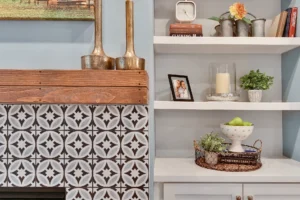 Farmhouse living room with tiled fireplace, wooden mantle, and white shelves decorated with cozy accents.
