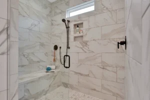 Luxurious white marble walk-in shower with black fixtures, built-in bench, and natural light.
