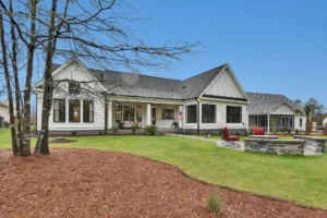 Modern farmhouse with white siding, patio seating, and circular stone fire pit in backyard.