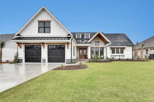 Modern white farmhouse with black trim, gable roof, wooden porch, and two-car garage.