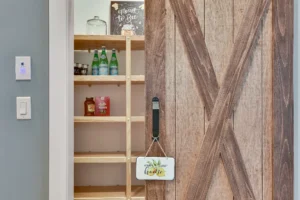 Rustic sliding barn door revealing organized farmhouse pantry with wood shelves and cozy modern charm.