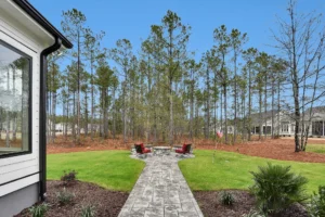 Peaceful backyard patio with stone path, red chairs, firepit, and pine tree view.