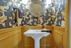 Chic powder room with white pedestal sink, golden koi wallpaper, and warm mustard paneling.