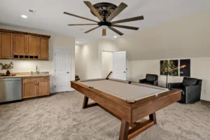 Modern game room with wooden pool table, ceiling fan, cozy seating, and stylish kitchenette.