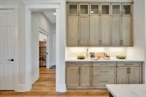 Modern beige kitchen with glass cabinets, white countertops, and warm wood flooring.