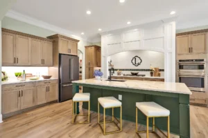Modern kitchen with forest green island, light wood cabinets, marble countertops, and stainless-steel appliances.