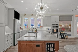 Modern gray kitchen with marble island, starburst chandeliers, and stainless steel appliances.