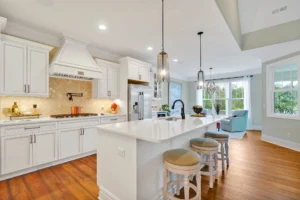 Bright modern white kitchen with large island, wood floors, and elegant pendant lighting.